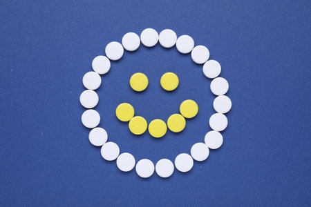 Happy face made of antidepressant pills on dark blue background, flat lay
