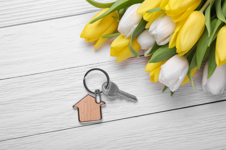 Beautiful spring flowers and key with trinket in shape of house on white wooden table, flat layの写真素材