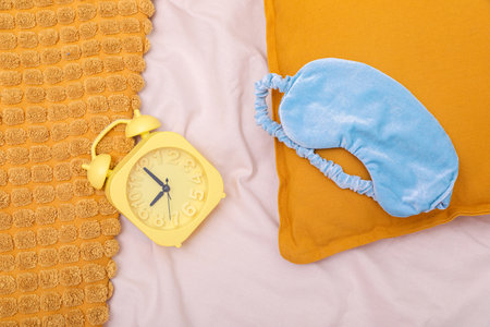 Light blue sleep mask, pillow and alarm clock on beige cloth, flat layの写真素材