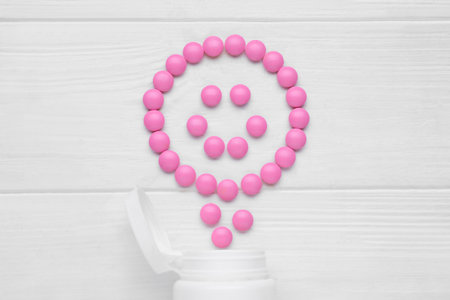 Happy emoticon made of pink antidepressants and medical jar on white wooden table, flat layの写真素材