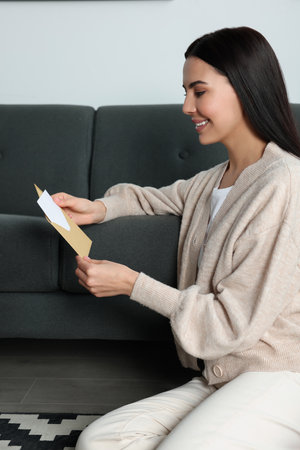 Happy woman reading greeting card on floor in living roomの写真素材
