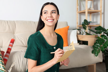 Happy woman writing message in greeting card on floor in living roomの写真素材