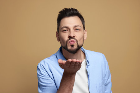 Handsome man blowing kiss on beige backgroundの写真素材