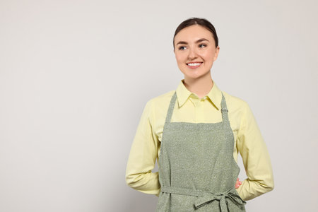 Beautiful young woman in clean apron with pattern on light gray background. Space for textの写真素材