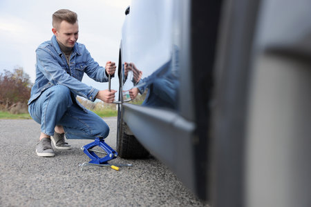 Young man changing tire of car on roadsideの写真素材