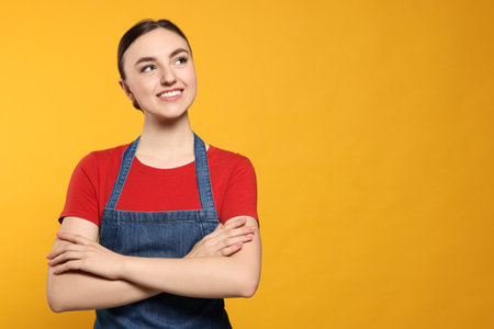 Beautiful young woman in clean denim apron on orange background. Space for textの写真素材