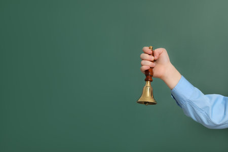 Pupil with school bell near green chalkboard, closeup. Space for textの写真素材