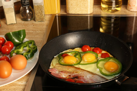 Cooking eggs with bacon, tomatoes and peppers in frying panの写真素材