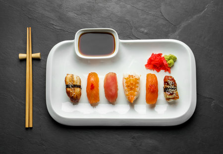 Plate with delicious nigiri sushi and soy sauce on black table, top viewの写真素材