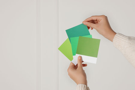 Woman with color sample cards choosing paint shade for wall indoors, closeup. interior designの写真素材