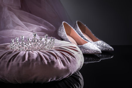 Pink pillow with beautiful silver tiara near shoes on black tableの写真素材