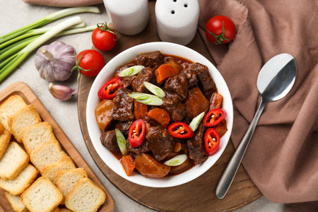 Delicious beef stew with carrots, chili peppers, green onions and potatoes served on white textured table, flat layの写真素材