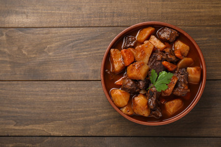 Delicious beef stew with carrots, parsley and potatoes on wooden table, top view. Space for textの写真素材
