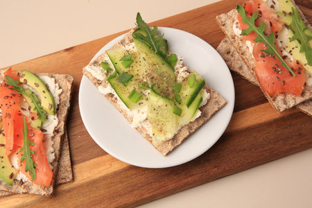Fresh crunchy crispbreads with cream cheese, cucumber, green onion, salmon and arugula on beige tableの写真素材