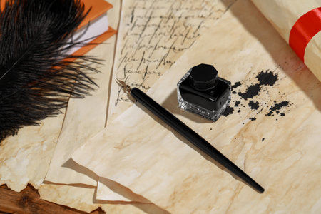 Inkwell, feather, fountain pen and vintage parchment on wooden table, above viewの写真素材