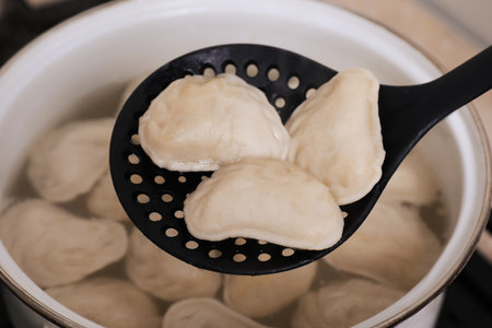 Dumplings (varenyky) with tasty filling on skimmer over pot, closeupの写真素材