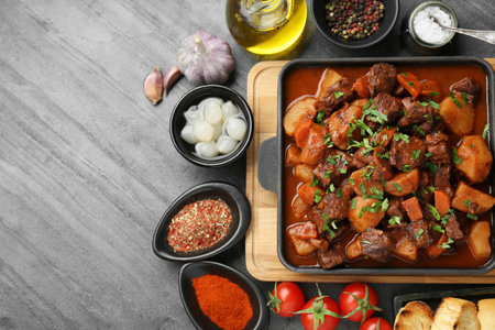 Delicious beef stew and ingredients on gray table, flat lay. Space for textの写真素材