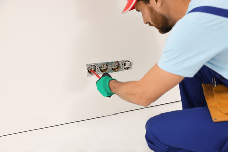 Electrician with screwdriver repairing power sockets indoors