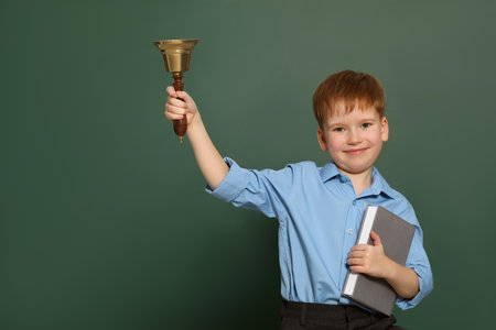 Pupil with school bell near green chalkboard. Space for textの写真素材