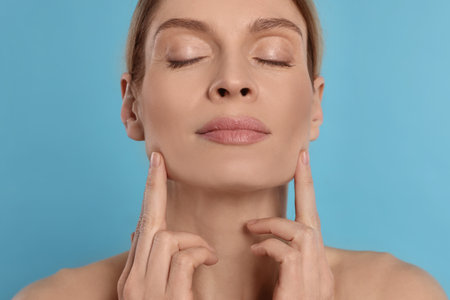 Woman massaging her face on turquoise backgroundの写真素材