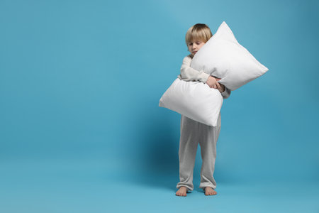 Boy in pajamas hugging pillow on light blue background, space for textの写真素材