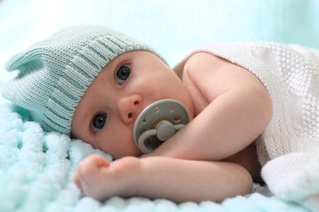 Cute newborn baby with pacifier on light blue blanket, closeup