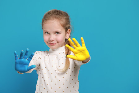 Little girl with hands painted in Ukrainian flag colors on light blue background, space for text. Love Ukraine conceptの写真素材