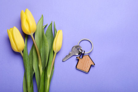 Beautiful spring flowers and key with trinket in shape of house on violet background, flat layの写真素材