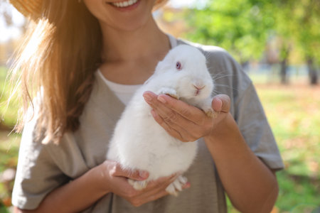 Happy woman holding cute white rabbit in park, closeupの写真素材