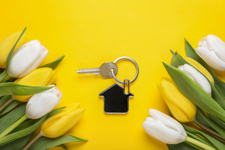 Beautiful spring flowers and key with trinket in shape of house on yellow background, flat layの写真素材