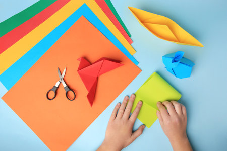 origami art. Child folding paper on light blue background, closeup and top viewの写真素材