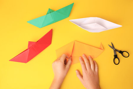 origami art. Child folding paper on yellow background, closeup and top viewの写真素材