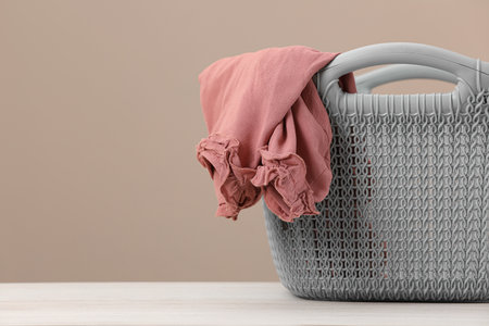 Plastic laundry basket with clothes near beige wall. Space for textの写真素材