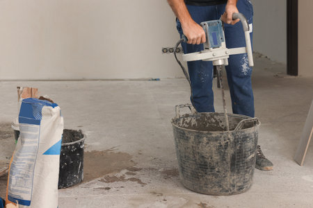 Professional worker mixing cement in bucket indoors, closeup. Tiles installation processの写真素材