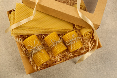 Beautiful yellow beeswax candles and sheets in box on light textured table, top viewの写真素材