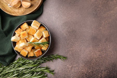 Delicious crispy croutons in bowl and rosemary on dark table, flat lay. Space for textの写真素材