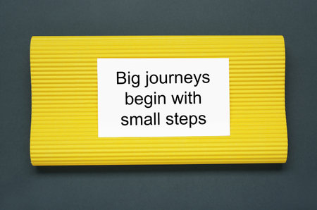 Card with phrase Big Journeys Begin With Small Steps on dark background, top view. Motivational...