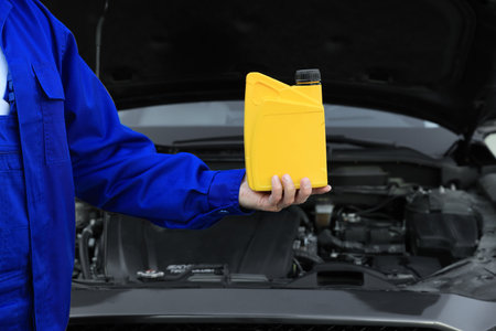 Worker holding yellow container of motor oil near modern car, closeupの写真素材