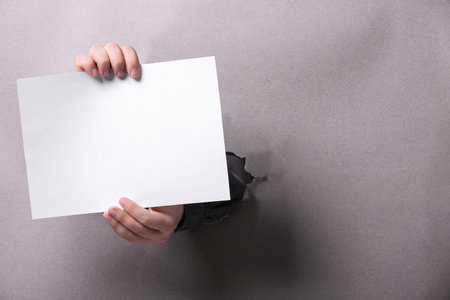 Man holding sheet of paper through hole in white paper, closeup. Mockup for designの写真素材