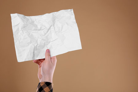 Man holding sheet of crumpled paper on pale orange background, closeup. Mockup for design