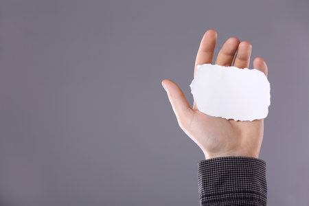 Man holding sheet of torn paper on gray background, closeup. Mockup for designの写真素材