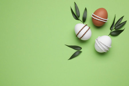 Beautifully decorated Easter eggs and leaves on light green background, flat lay. Space for textの写真素材