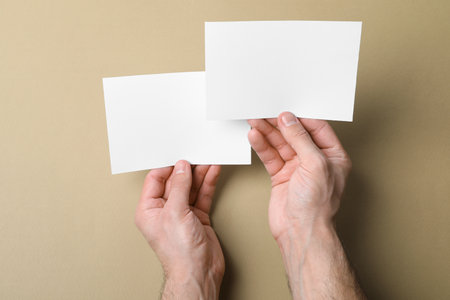 Man holding flyers on light brown background, top view. Mockup for designの写真素材