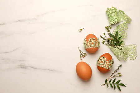 Flat lay composition with Easter eggs, twigs and lace ribbon on white marble table. Space for text
