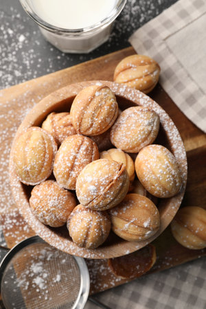 Delicious nut shaped cookies with powdered sugar and milk on black table, flat layの写真素材