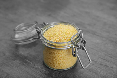 Glass jar of raw couscous on gray table, closeupの写真素材