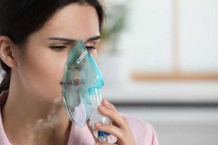 Sick young woman using nebulizer at home, closeup. Space for textの写真素材
