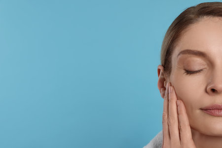 Woman massaging her face on turquoise background, closeup. Space for textの写真素材
