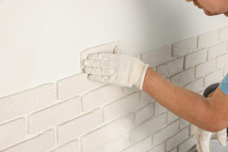 Worker installing decorative wall tiles in room, closeupの写真素材