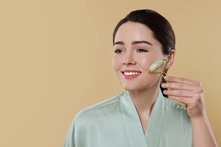 Young woman massaging her face with jade roller on beige background. Space for textの写真素材